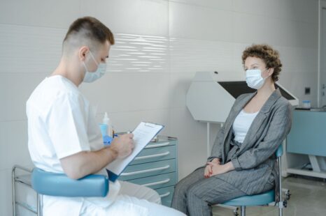 Doctor consulting a masked patient about rhinoplasty risks in clinic