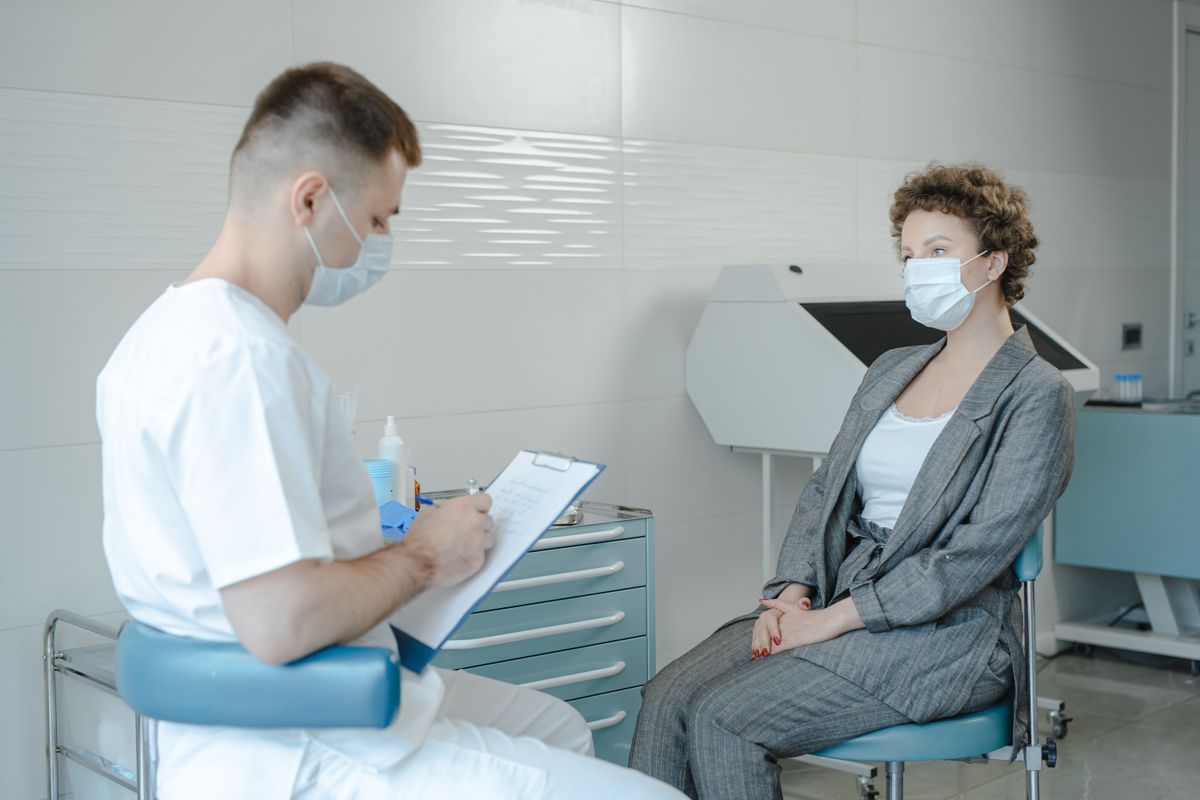Doctor consulting a masked patient about rhinoplasty risks in clinic
